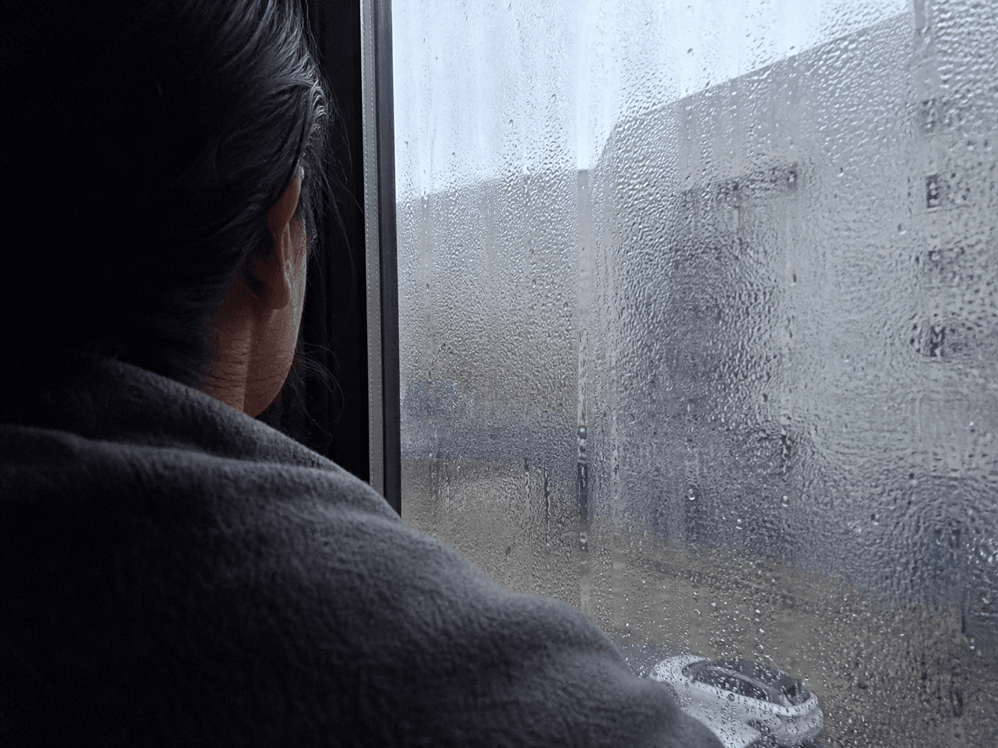 Buğulu bir pencereden dışarıya dalıp giden bir kişinin omuz arkasından görünümü