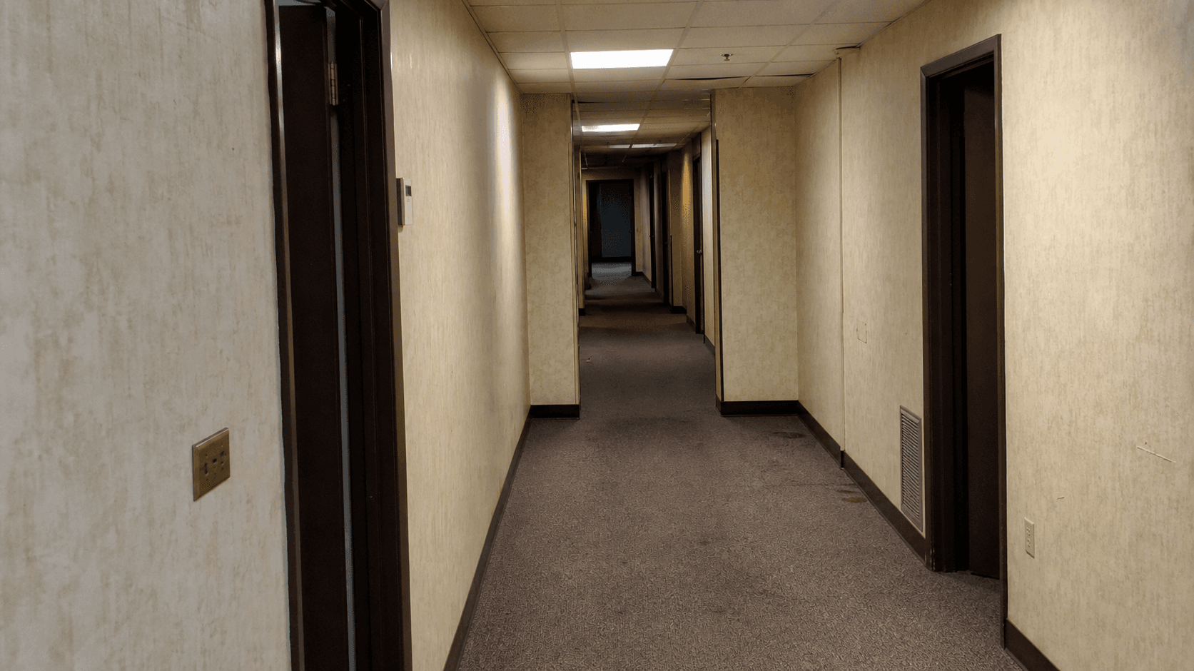 Sarı duvarlı, floresan ışıklı ve boş görünen eski bir ofis koridoru